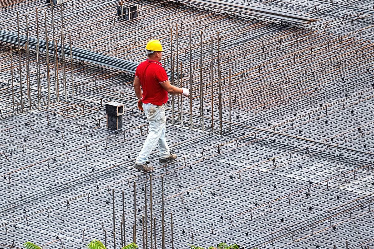 Ouvrier casqué marchant sur les armatures métalliques d'une dalle en cours de coulage sur un chantier